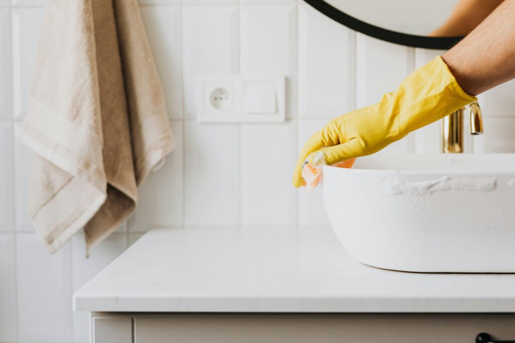 pexels-photo-4239116-4239116 Crop anonymous person wearing yellow latex gloves washing sink in bathroom with orange sponge and cleanser while cleaning contemporary flat